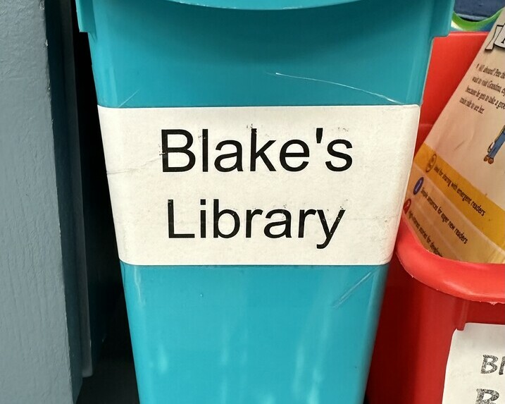 A plastic bin labelled, "Blake's Library" sits on a shelf in a classroom