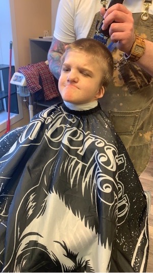 The student sits up straight while a barber trims the top of his hair. 